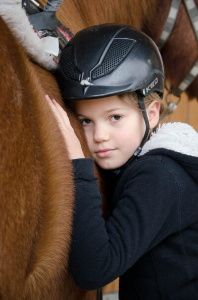 Mädchen schmiegt sich an ein Pony Ein Mädchen mit Reithelm legt Wange und Hand an den Hals eines braunen Ponys und blickt in die Kamera